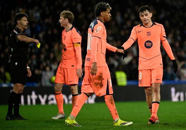 Barcelona's Spanish midfielder #08 Pedri and Barcelona's Spanish forward #10 Lamine Yamal (2R) shake hands as Spanish referee Jesus Gil (L) presents a yellow card to FC Porto's Dutch forward #26 Luuk De Jong during the Spanish league football match between Real Sociedad and FC Barcelona at Anoeta Stadium in San Sebastian on January 18, 2026. (Photo by ANDER GILLENEA / AFP)