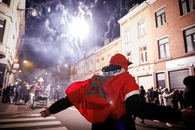 A supporter with a Moroccan national flag gestures near fireworks going off in a street in Brussels, on January 18, 2026 following the Africa Cup of Nations (AFCON) final football match between Senegal and Morocco played in Rabat, Morocco. Senegal won the Africa Cup of Nations as Pape Gueye's extra-time winner sunk hosts Morocco 1-0 after a chaotic final that saw the eventual champions storm off the pitch late in the game. (Photo by Simon Wohlfahrt / AFP)