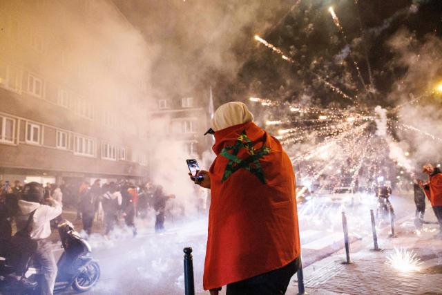 A supporter with a Moroccan national stands near fireworks going off in a street in Brussels, on January 18, 2026 following the Africa Cup of Nations (AFCON) final football match between Senegal and Morocco played in Rabat, Morocco. Senegal won the Africa Cup of Nations as Pape Gueye's extra-time winner sunk hosts Morocco 1-0 after a chaotic final that saw the eventual champions storm off the pitch late in the game. (Photo by Simon Wohlfahrt / AFP)