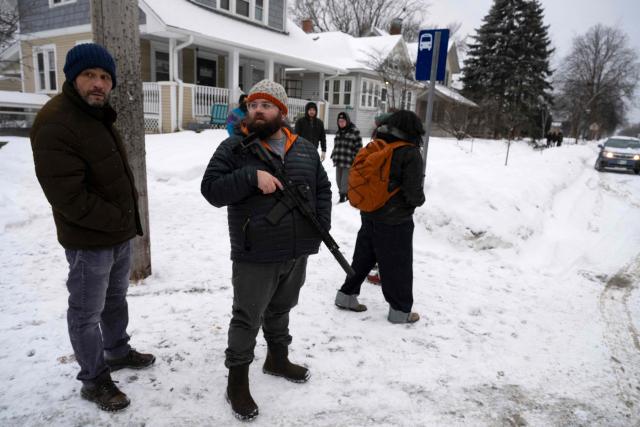A resident of a neighborhood in Falcon Heights, Minnesota, holds an AR-15 assault rifle as he and other neighbors came out from their homes after spotting what they believe to be US Immigration and Customs Enforcement (ICE) agents on January 18, 2026. Crowds of protesters have clashed with immigration officers across Minneapolis, opposing their efforts to target undocumented migrants. Some officers have responded with violence. Demonstrations grew dramatically following the fatal shooting of Renee Nicole Good as the Trump administration pressed operations to catch undocumented migrants. (Photo by ROBERTO SCHMIDT / AFP)