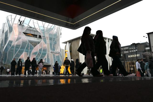 People walk at a business district in Beijing on January 18, 2026. (Photo by WANG Zhao / AFP)