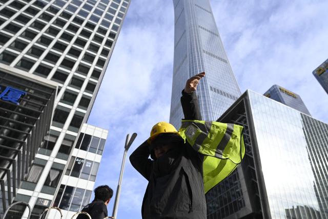 A worker wears his vest as he prepares to enter a construction site the a Central Business District (CBD) in Beijing on January 19, 2026. (Photo by WANG Zhao / AFP)