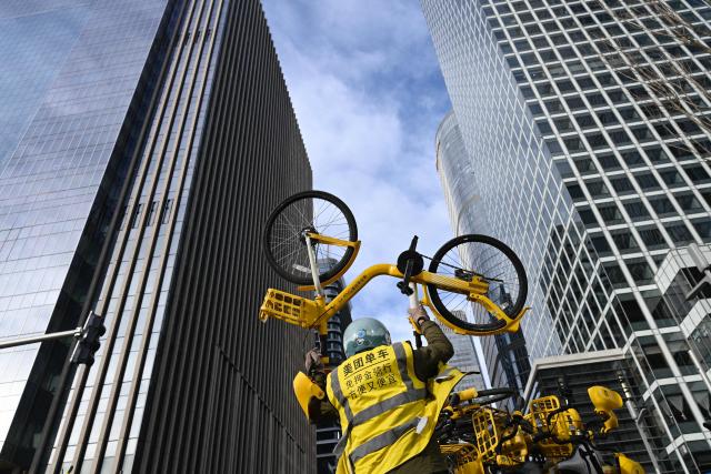 A worker loads sharing bicycles at the Central Business District (CBD) in Beijing on January 19, 2026. (Photo by WANG Zhao / AFP)