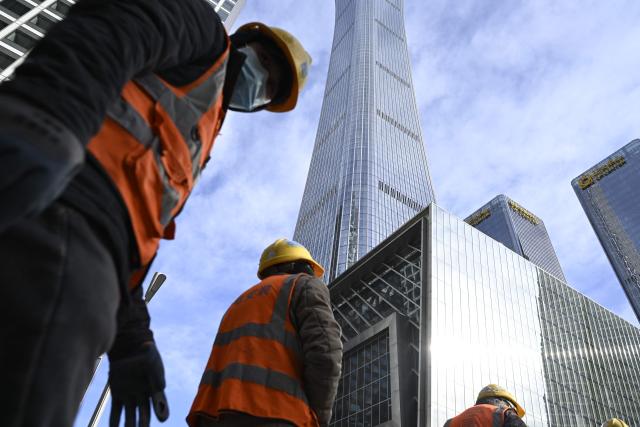 A group of workers walk out an construction site at the Central Business District (CBD) in Beijing on January 19, 2026. (Photo by WANG Zhao / AFP)