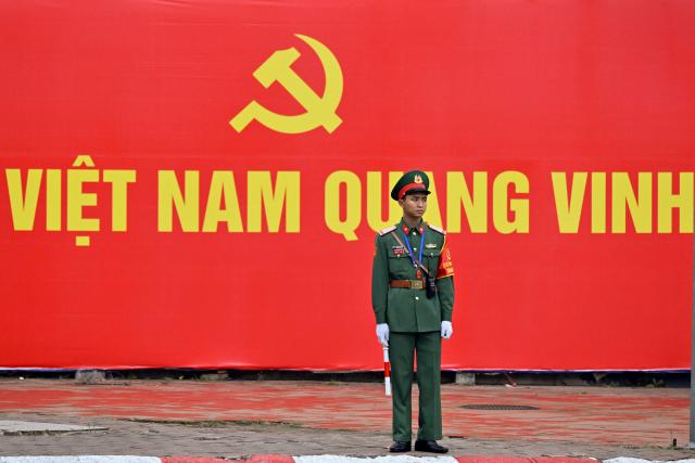 A soldier stands in front of a billboard for the 14th Congress of the Communist Party of Vietnam outside the National Convention Center in Hanoi on January 19, 2026. Vietnam's ruling Communist Party convened on January 19 to begin their twice-a-decade congress, where leader To Lam is looking to tighten his grip on power less than two years after assuming the top role. (Photo by Nhac NGUYEN / AFP)