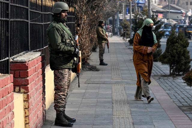 A woman walks past Indian paramilitary troopers standing guard along a roadside in Srinagar on January 19, 2026 as security measures tighten ahead of India's Republic Day celebrations. (Photo by Tauseef MUSTAFA / AFP)