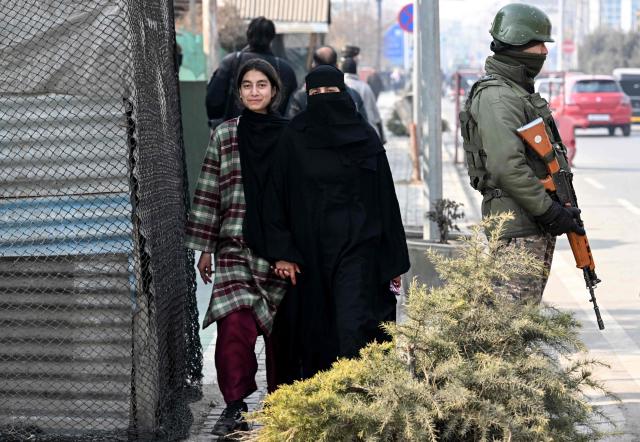 Pedestrians walk past an Indian paramilitary trooper standing guard along a roadside in Srinagar on January 19, 2026 as security measures tighten ahead of India's Republic Day celebrations. (Photo by Tauseef MUSTAFA / AFP)