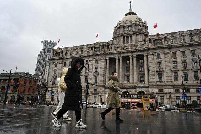People walk past the Shanghai Pudong Development Bank located on the Bund in Shanghai on January 19, 2026. China's economy grew at one of the slowest rates in decades last year, according to official data released on January 19, as officials struggle to overcome persistently low consumer spending and a debt crisis in the country's property sector. (Photo by Jade GAO / AFP)