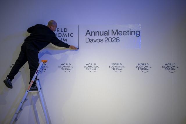 EDITORS NOTE: Graphic content / A staff members fixes a sign on a wall of the World Economic Forum (WEF) at the Congress Centre on its opening day in Davos on January 19, 2026. The World Economic Forum takes place in Davos from January 19 to January 23, 2026. (Photo by Fabrice COFFRINI / AFP)