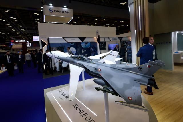 Visitors walk past a model of Qatar's fighter jet on display during the Doha International Maritime Defence Exhibition and Conference (DIMDEX 2026) which showcases technology, maritime, and defence capabilities, at the Qatar National Convention Centre, in Doha on January 19, 2026. (Photo by Karim JAAFAR / AFP)