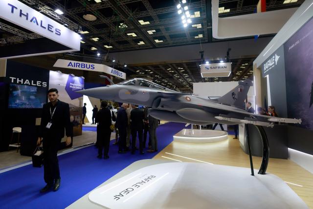 Visitors walks past a model of Qatar's fighter jet on display during the Doha International Maritime Defence Exhibition and Conference (DIMDEX 2026) which showcases technology, maritime, and defence capabilities, at the Qatar National Convention Centre, in Doha on January 19, 2026. (Photo by Karim JAAFAR / AFP)