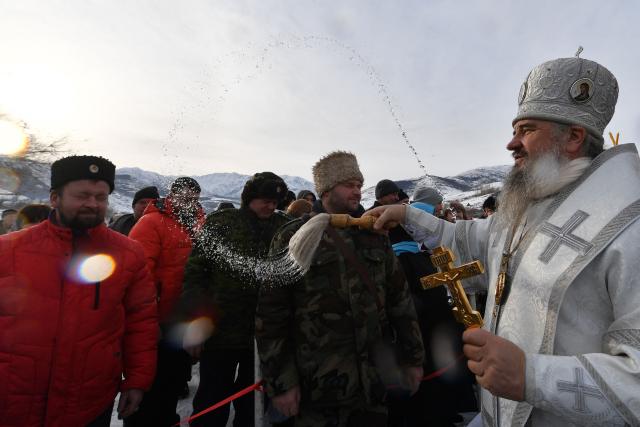 An Orthodox priest blesses believers during the Epiphany holiday near the village of Sosnovka, northern Kyrgyzstan on January 19, 2026. (Photo by Vyacheslav OSELEDKO / AFP)