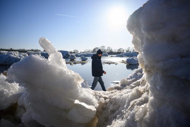 A passerby walks past large chunks of ice washed up along the banks of the Elbe river near Geesthacht, northern Germany, on January 19, 2026. Following several days of freezing winter temperatures and a low water level, ground ice started to form and to emerge to the surface. (Photo by DANIEL REINHARDT / AFP)