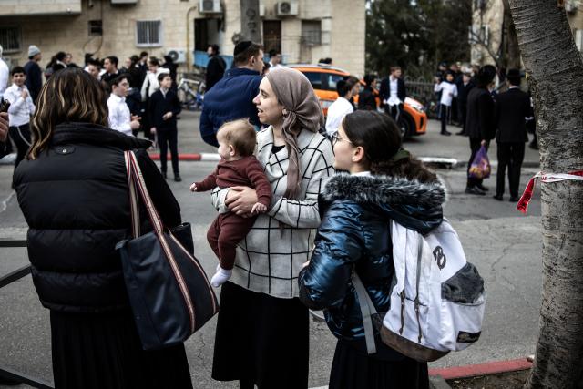 A woman holds her baby at the site where faulty heating system left two babies dead and many others injured at a day care in Jerusalem on January 19, 2026. Israeli doctors declared two babies dead after medics evacuated 55 children from a daycare centre in Jerusalem on January 19, with local media reporting the incident may have been linked to the facility's heating system. (Photo by JOHN WESSELS / AFP)