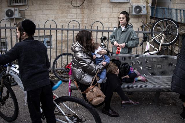 A woman holds her baby at the site where faulty heating system left two babies dead and many others injured at a day care in Jerusalem on January 19, 2026. Israeli doctors declared two babies dead after medics evacuated 55 children from a daycare centre in Jerusalem on January 19, with local media reporting the incident may have been linked to the facility's heating system. (Photo by JOHN WESSELS / AFP)