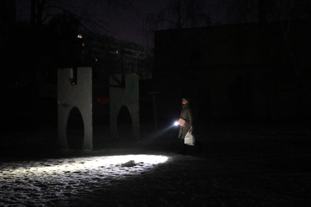 A woman using a flashlight walks through an unlit courtyard of a residential building during a power outage in Kyiv on January 19, 2026, amid the Russian invasion of Ukraine. Russian attacks have left Ukraine's energy grid teetering on the brink of collapse and have disrupted power and water supplies to millions over recent weeks. (Photo by Sergei GAPON / AFP)