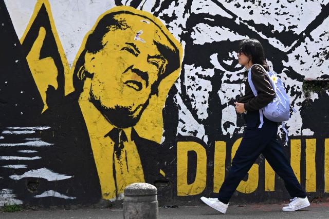 A woman walks past an anti-immigration-policy graffiti depicting US President Donald Trump in Bogota on January 18, 2026.  (Photo by Raul ARBOLEDA / AFP)