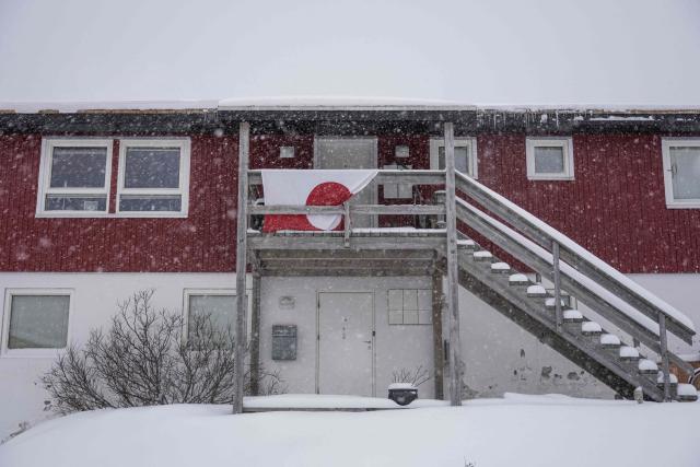 TOPSHOT - The Greenland flag hangs from a balcony of a residential building as snow falls in Nuuk, Greenland, on January 19, 2026. (Photo by Jonathan NACKSTRAND / AFP)