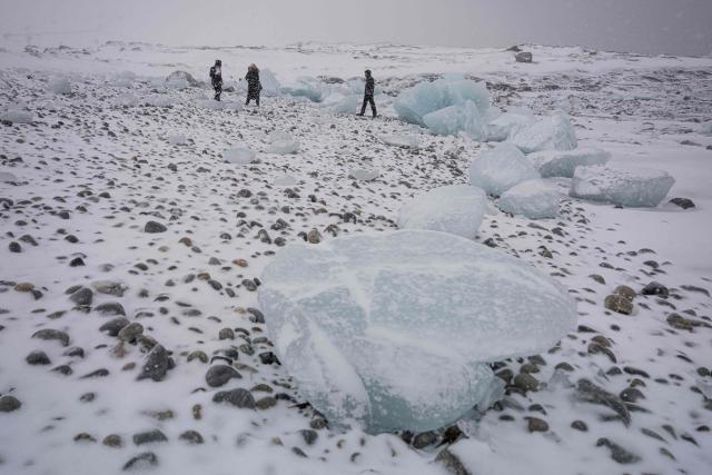 People walk along the shoreline past ice formations as snow falls in Nuuk, Greenland, on January 19, 2026. (Photo by Jonathan NACKSTRAND / AFP)
