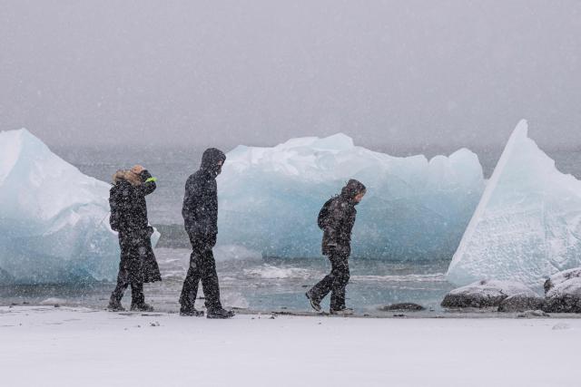 People walk along the shoreline past ice formations as snow falls in Nuuk, Greenland, on January 19, 2026. (Photo by Jonathan NACKSTRAND / AFP)