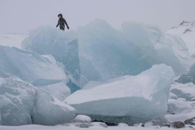 A woman walks along the shoreline past ice formations as snow falls in Nuuk, Greenland, on January 19, 2026. (Photo by Jonathan NACKSTRAND / AFP)