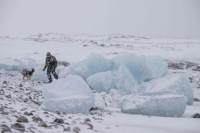 A man walks his dog along the shoreline past ice formations as snow falls in Nuuk, Greenland, on January 19, 2026. (Photo by Jonathan NACKSTRAND / AFP)