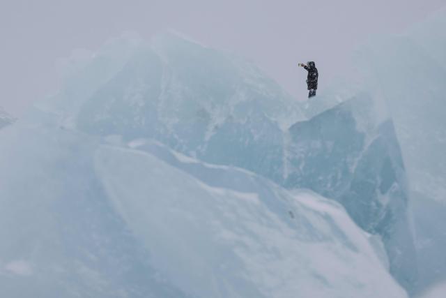 TOPSHOT - A man takes a picture as he walks along the shoreline past ice formations as snow falls in Nuuk, Greenland, on January 19, 2026. (Photo by Jonathan NACKSTRAND / AFP)