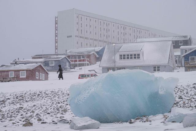 A woman walks close to the shoreline past ice formations as snow falls in Nuuk, Greenland, on January 19, 2026. (Photo by Jonathan NACKSTRAND / AFP)