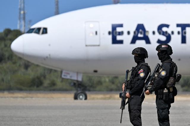 Members of the Bolivarian National Intelligence Service guard an Eastern Airlines plane carrying Venezuelan migrants deported from the United States as it arrives at Simon Bolivar International Airport in Maiquetia, Venezuela on January 19, 2026. (Photo by Juan BARRETO / AFP)