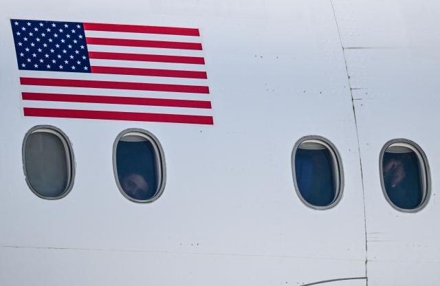 Venezuelan migrants deported from the United States look out the windows and show their hands in chains and handcuffs aboard an Eastern Airlines plane upon arrival at Simon Bolivar International Airport in Maiquetia, Venezuela on January 19, 2026. (Photo by Juan BARRETO / AFP)