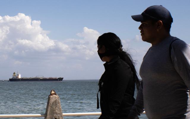 A couple walks with the Panamanian tanker CH Alquimia in the background on Lake Maracaibo in Maracaibo, Venezuela, on January 18, 2026. (Photo by Margioni BERMÚDEZ / AFP)