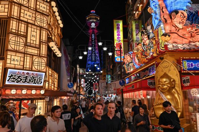 (FILES) This photo taken on September 30, 2025 shows tourists visiting the main crossroads of the popular Shinsekai area in Naniwa ward as Tsutenkaku Tower (C) looms in the background in Osaka. A record numbers of visitors flocked to Japan last year, the transport ministry said on January 20, 2026, as the weak yen bolstered its appeal. (Photo by Richard A. Brooks / AFP)