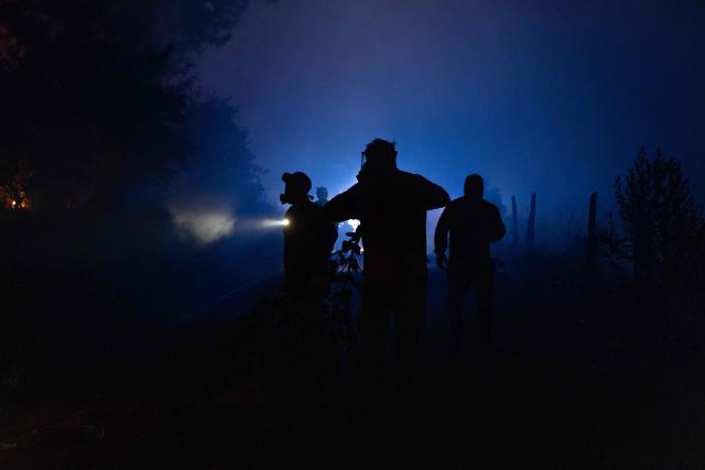 People gather to try to extinguish burning vegetation during a wildfire in the town of Florida near the city of Concepción, Chile, on January 19, 2026. Wildfires that have killed 19 people in southern Chile and wiped out entire towns, raged for a third day on January 19, fanned by high temperatures and strong winds at the height of the southern hemisphere summer. (Photo by Raul BRAVO / AFP)