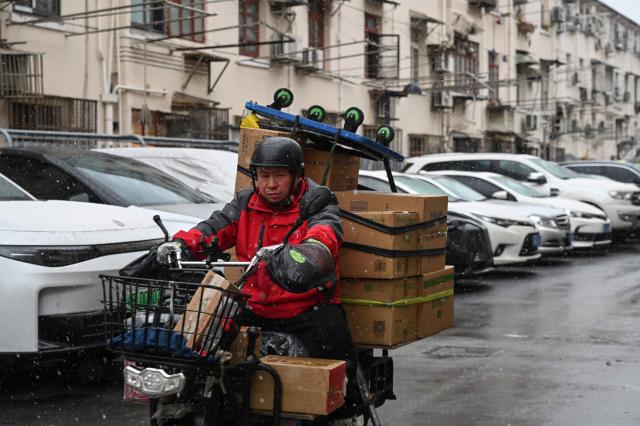 A delivery man rides a scooter at a residential compound during a snowy day in Shanghai on January 20, 2026. (Photo by Jade GAO / AFP)