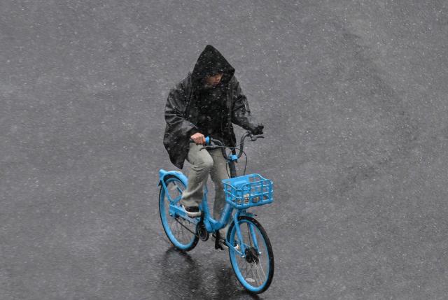 A man rides a bicycle on a street during a snowy day in Shanghai on January 20, 2026. (Photo by Hector RETAMAL / AFP)