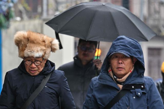 People walk on a street during a snowy day in Shanghai on January 20, 2026. (Photo by Hector RETAMAL / AFP)