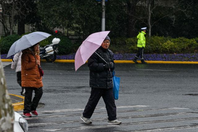 People walk on a street during a snowy day in Shanghai on January 20, 2026. (Photo by Hector RETAMAL / AFP)