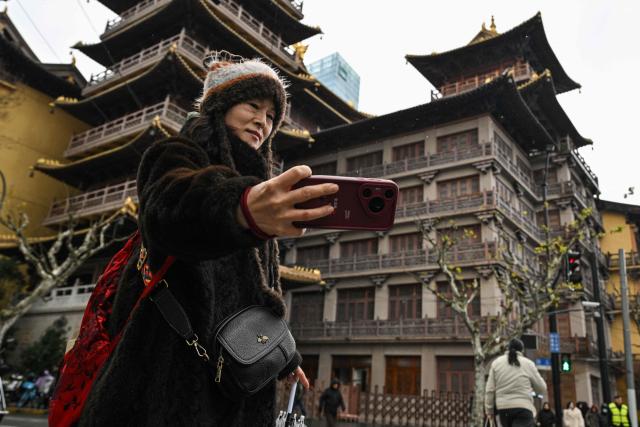 A woman takes a selfie on a street next to Jing'an temple during a snowy day in Shanghai on January 20, 2026. (Photo by Hector RETAMAL / AFP)
