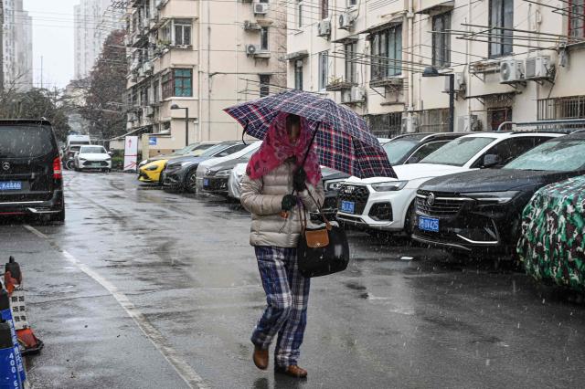 A woman uses an umbrella to shelter from snow at a residential compound during a snowy day in Shanghai on January 20, 2026. (Photo by Jade GAO / AFP)