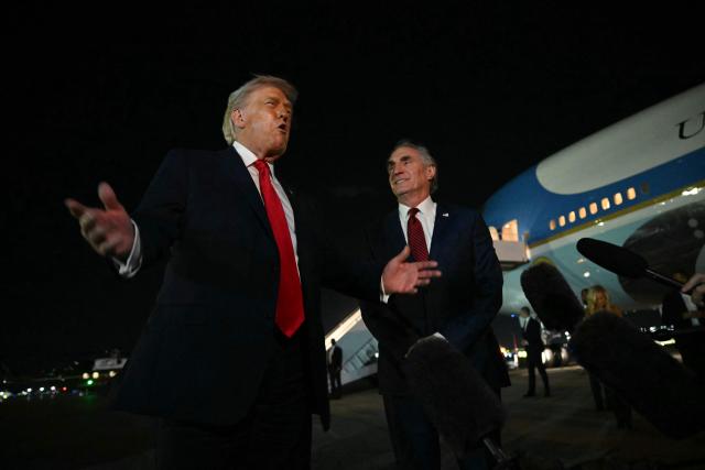 US President Donald Trump speaks with reporters as the Secretary of the Interior Doug Burgum (R) looks on, before boarding Air Force One at Palm Beach International Airport, in West Palm Beach, Florida on January 19, 2026. President Trump is returning to Washington after spending the weekend at his Mar-a-Lago residence and attending the College Football National Championship Game between Miami Hurricanes and Indiana Hoosiers at Hard Rock Stadium in Miami Gardens, Florida. (Photo by ANDREW CABALLERO-REYNOLDS / AFP)