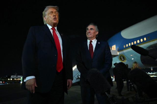 US President Donald Trump speaks with reporters as the Secretary of the Interior Doug Burgum (R) looks on, before boarding Air Force One at Palm Beach International Airport, in West Palm Beach, Florida on January 19, 2026. President Trump is returning to Washington after spending the weekend at his Mar-a-Lago residence and attending the College Football National Championship Game between Miami Hurricanes and Indiana Hoosiers at Hard Rock Stadium in Miami Gardens, Florida. (Photo by ANDREW CABALLERO-REYNOLDS / AFP)