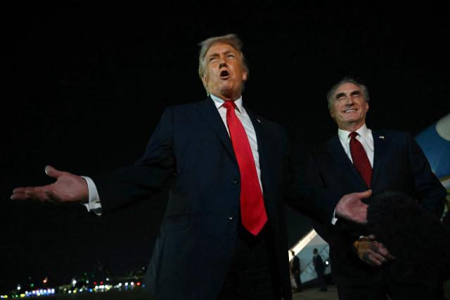 US President Donald Trump speaks with reporters as the Secretary of the Interior Doug Burgum (R) reacts, before boarding Air Force One at Palm Beach International Airport, in West Palm Beach, Florida on January 19, 2026. President Trump is returning to Washington after spending the weekend at his Mar-a-Lago residence and attending the College Football National Championship Game between Miami Hurricanes and Indiana Hoosiers at Hard Rock Stadium in Miami Gardens, Florida. (Photo by ANDREW CABALLERO-REYNOLDS / AFP)