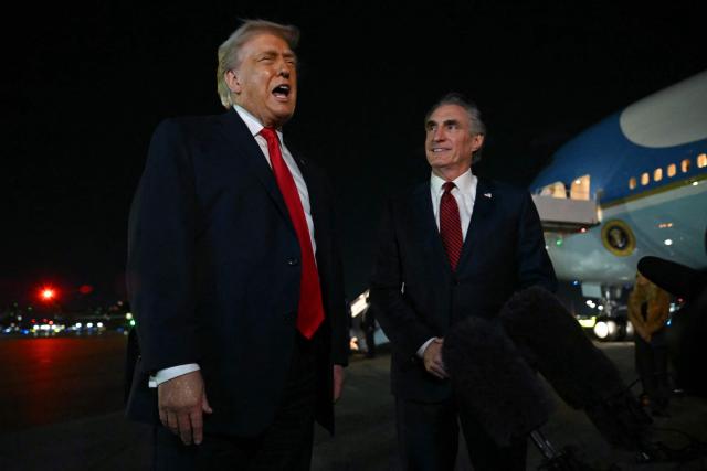 US President Donald Trump speaks with reporters as the Secretary of the Interior Doug Burgum (R) looks on, before boarding Air Force One at Palm Beach International Airport, in West Palm Beach, Florida on January 19, 2026. President Trump is returning to Washington after spending the weekend at his Mar-a-Lago residence and attending the College Football National Championship Game between Miami Hurricanes and Indiana Hoosiers at Hard Rock Stadium in Miami Gardens, Florida. (Photo by ANDREW CABALLERO-REYNOLDS / AFP)