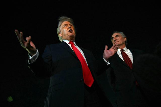 US President Donald Trump speaks with reporters as the Secretary of the Interior Doug Burgum (R) looks on, before boarding Air Force One at Palm Beach International Airport, in West Palm Beach, Florida on January 19, 2026. President Trump is returning to Washington after spending the weekend at his Mar-a-Lago residence and attending the College Football National Championship Game between Miami Hurricanes and Indiana Hoosiers at Hard Rock Stadium in Miami Gardens, Florida. (Photo by ANDREW CABALLERO-REYNOLDS / AFP)