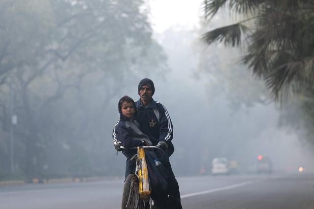 A man with his child rides a bicycle to school amid smoggy conditions in New Delhi on January 20, 2026. (Photo by Manan VATSYAYANA / AFP)