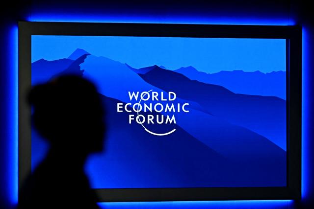 The logo of the World Economic Forum is displayed on a big screen as a visitor is silhouetted during the World Economic Forum (WEF) annual meeting in Davos on January 20, 2026. The World Economic Forum takes place in Davos from January 19 to January 23, 2026. (Photo by Fabrice COFFRINI / AFP)