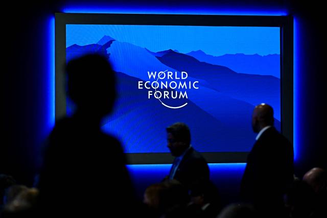 The logo of the World Economic Forum is displayed on a big screen as visitors are silhouetted during the World Economic Forum (WEF) annual meeting in Davos on January 20, 2026. The World Economic Forum takes place in Davos from January 19 to January 23, 2026. (Photo by Fabrice COFFRINI / AFP)