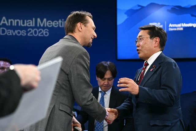 Japan's Minister of Economy, Trade and Industry Ryosei Akazawa (R) shakes hands with European Economics commentator for the Financial Times Martin Sandbu during the World Economic Forum (WEF) annual meeting in Davos on January 20, 2026. The World Economic Forum takes place in Davos from January 19 to January 23, 2026. (Photo by Fabrice COFFRINI / AFP)