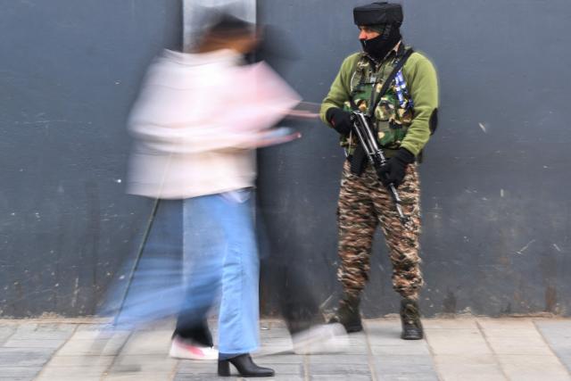 An Indian paramilitary trooper stands guard as pedestrians walks along a street in Srinagar on January 20, 2026, as security measures tighten ahead of India's Republic Day celebrations. (Photo by Tauseef MUSTAFA / AFP)