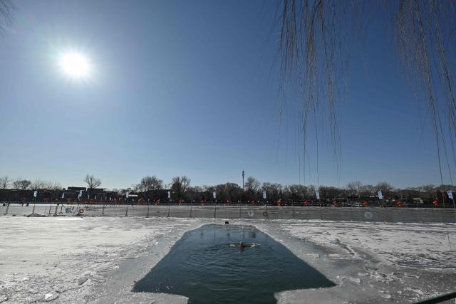 A winter swimming enthusiast swims at the Houhai Lake of the Shichahai scenic area in Beijing on January 20, 2026. Every winter dozens of locals add to their daily routine a frigid lap in the icy waters of Shichahai, a sprawling lake in the center of the Chinese capital. (Photo by Adek BERRY / AFP)